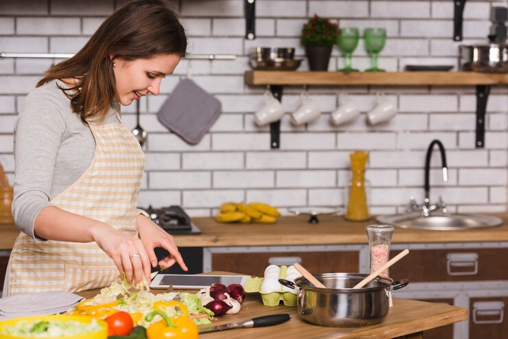 Gratis Foto vrouw die tablet gebruikt terwijl het koken van groenten