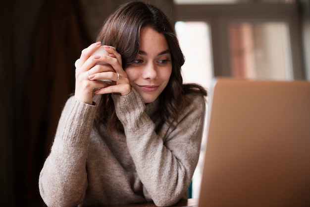 Vrouw die terwijl het houden van kop en het bekijken laptop glimlacht