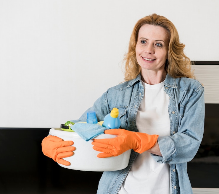Gratis Foto vrouw die terwijl het houden van mand schoonmakende producten stellen