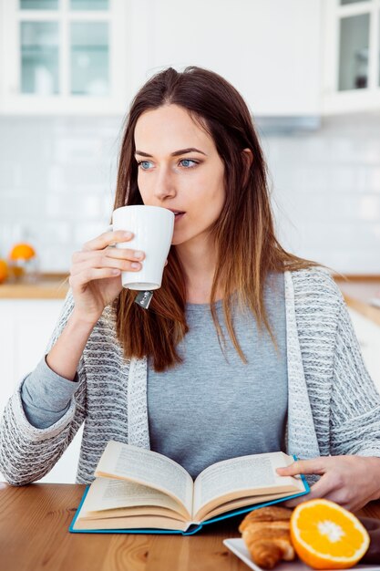 Vrouw die terwijl het lezen van boek drinkt