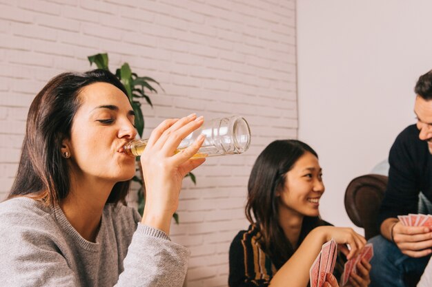 Vrouw die terwijl het spelen van kaartenspel drinken