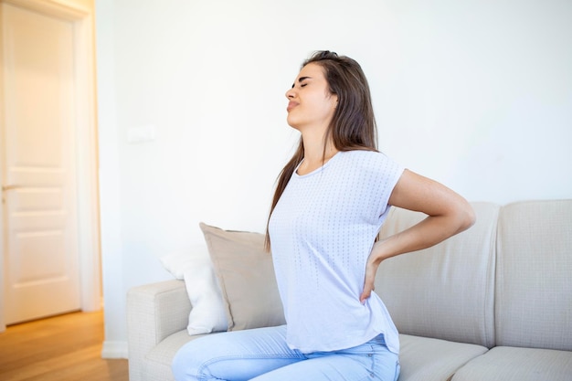 Vrouw die thuis aan rugpijn lijdt Lage rugpijn Vrouw voelt rugpijn die pijnlijke spieren masseert Trieste vrouw lijdt aan lage rug