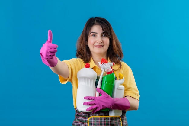 Vrouw die van middelbare leeftijd schort en rubberhandschoenen draagt die schoonmakende levering houden