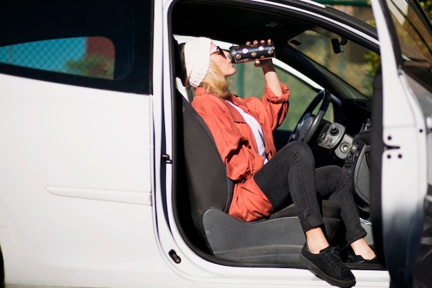 Vrouw die van thermosflessen in auto drinken
