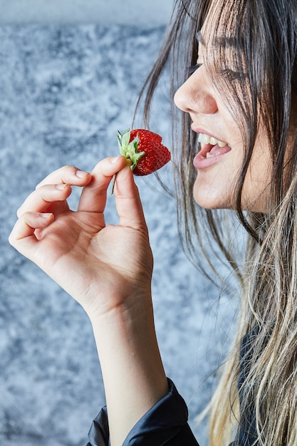 Gratis foto vrouw die verse rode aardbei op marmeren oppervlakte eet