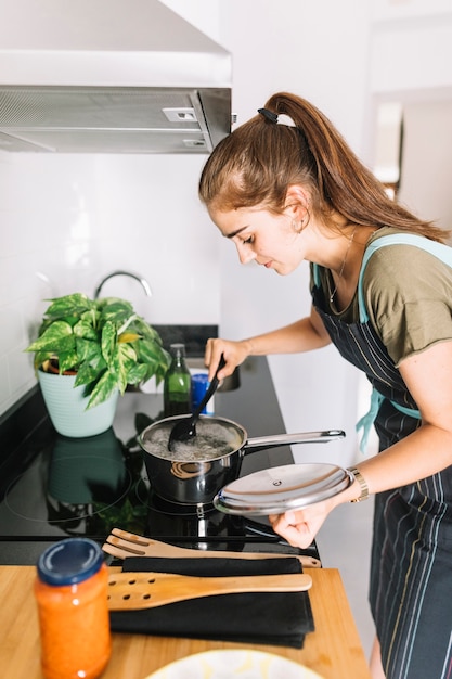 Vrouw die voedsel in steelpan over elektrisch fornuis voorbereidt