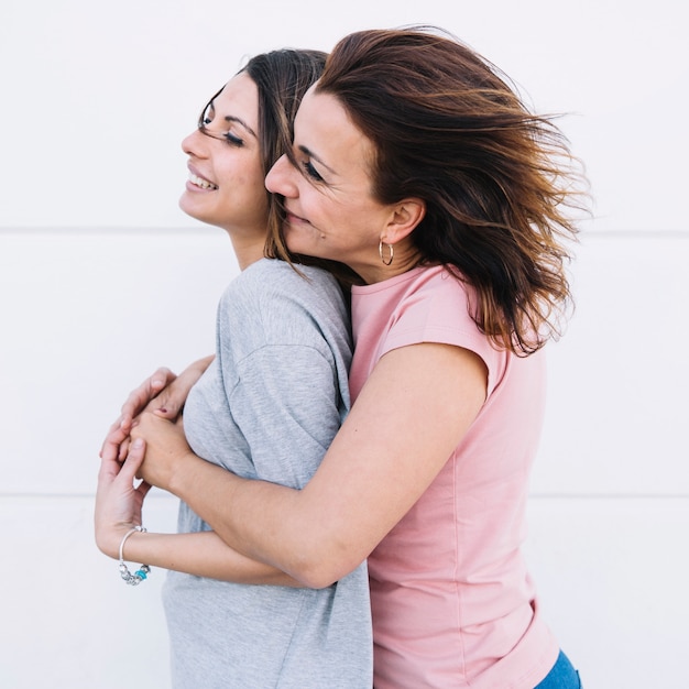 Vrouw die vrouw omhelzen dichtbij witte muur