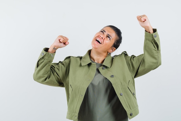 vrouw die winnaargebaar in jasje, t-shirt toont en gelukkig kijkt