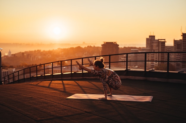 Vrouw die yoga op het dak van een wolkenkrabber in grote stad doet.