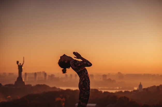 Vrouw die yoga op het dak van een wolkenkrabber in grote stad doet.