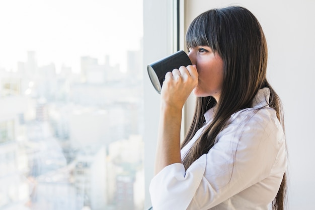 Vrouw die zich dichtbij de venster het drinken koffie bevindt