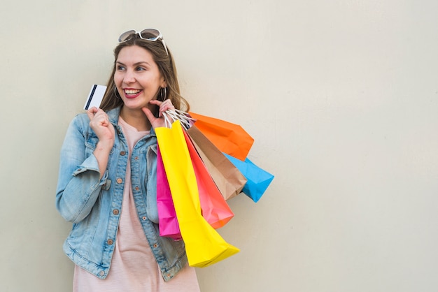 Gratis foto vrouw die zich met het winkelen zakken en creditcard bij lichte muur bevindt