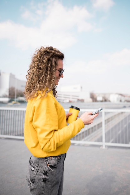 Gratis foto vrouw die zich zijdelings houdend een kop van koffie bevindt