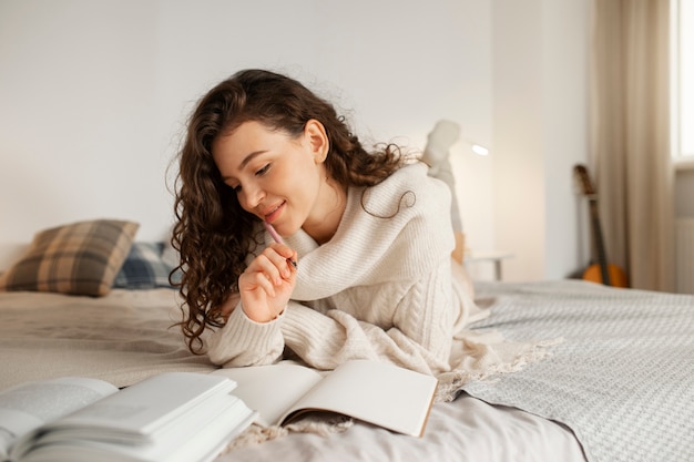 Gratis foto vrouw digitaal loskoppelen thuis door boek in bed te lezen