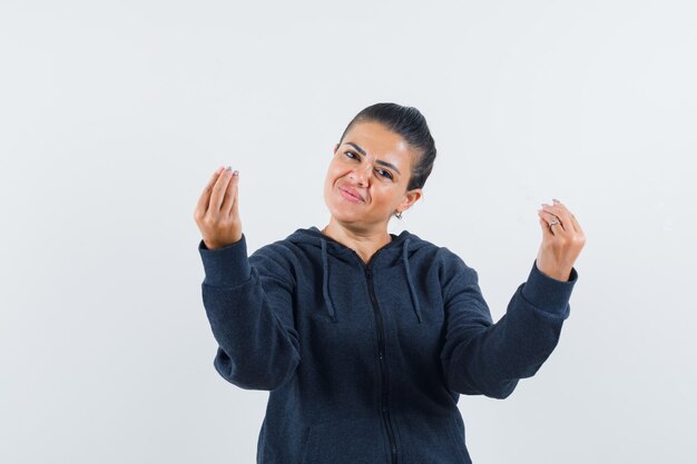 Vrouw doet Italiaans gebaar in hoodie en kijkt vrolijk, vooraanzicht.