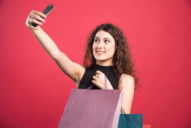 Vrouw doet selfie met tassen op rood.