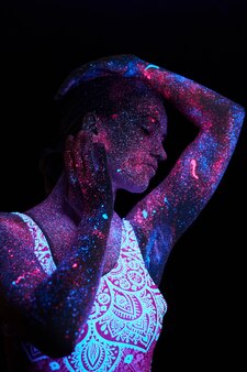 Vrouw doet yoga, handbewegingen, lichaamsopwarming. kunstmeisje kosmos in ultraviolet licht. het hele lichaam is bedekt met gekleurde druppels. astrale yoga