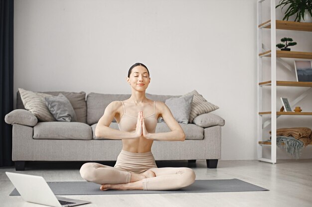 Vrouw doet yoga terwijl ze thuis online workout-tutorials op laptop bekijkt