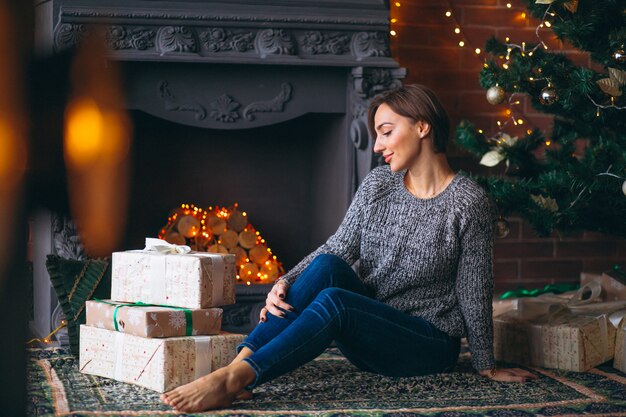 Vrouw door kerstboom presenteert uitpakken