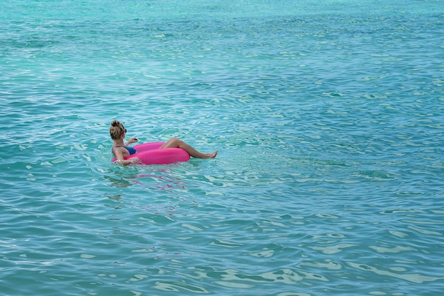 Vrouw draagt een bikini in een roze vlotter in de zee