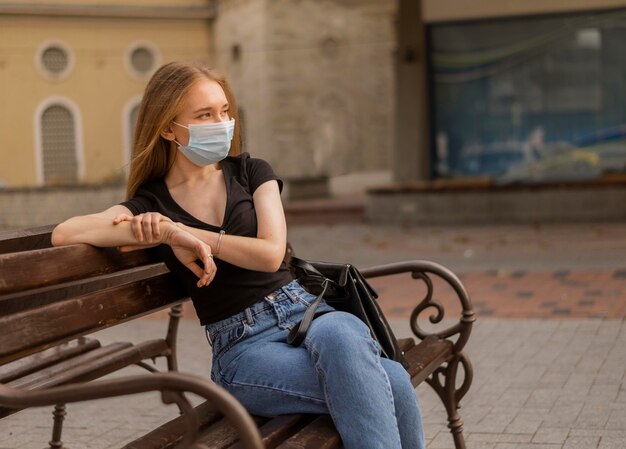Vrouw draagt een medisch masker buiten zittend op een bankje