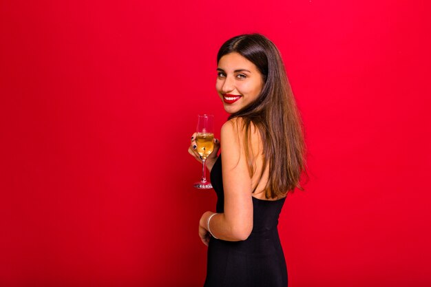 vrouw draagt een zwarte jurk en houdt een glas champagne poseren op rood