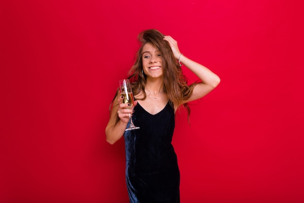 Vrouw draagt een zwarte jurk en houdt een glas champagne poseren op rood
