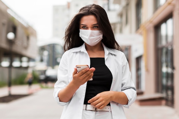 Vrouw draagt masker op weg naar haar werk terwijl ze naar smartphone kijkt