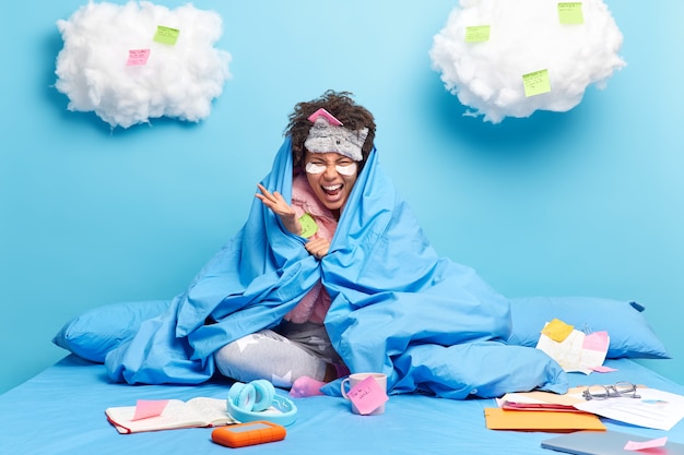 Vrouw draagt slaapmasker nachtkleding gebaren boos in deken gewikkeld beu van afstandsonderwijs heeft deadline om alle taken af te maken poseert alleen op bed