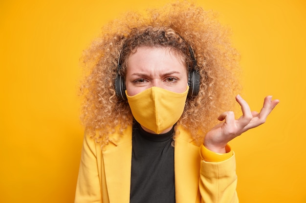 Gratis foto vrouw draagt stereo koptelefoon om naar muziek te luisteren beschermend gezichtsmasker tegen coronavirus steekt hand aarzelend op