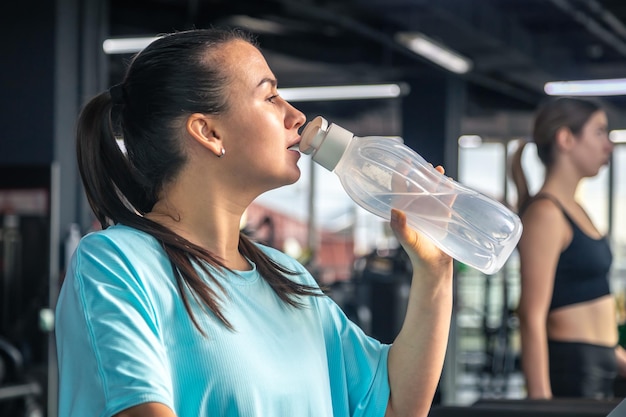 Vrouw drinkt water na het trainen op de loopband in de sportschool