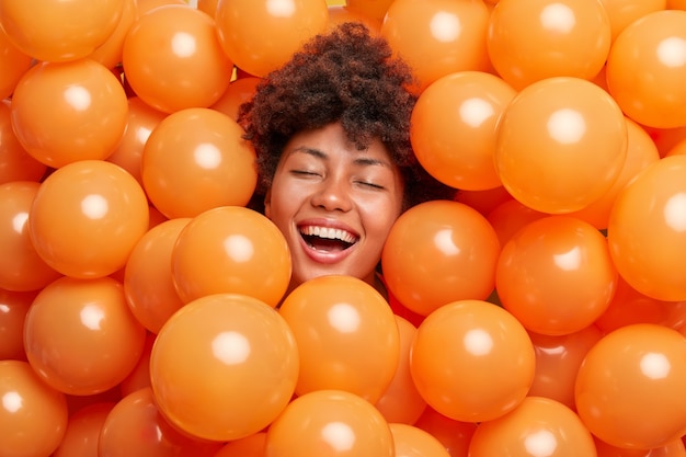 vrouw drukt positieve emoties uit houdt ogen gesloten glimlacht breed omringd door opgeblazen ballonnen