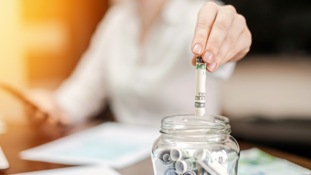 Vrouw een bankbiljetten te laten vallen in een pot met opgerolde bankbiljetten op tafel. Papieren op tafel