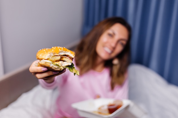 Vrouw eet hamburger thuis