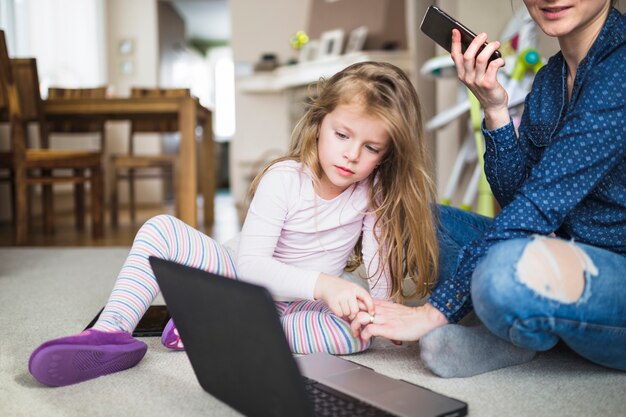 Vrouw en haar kind zittend op tapijt met mobiel en laptop