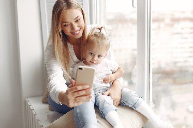 Vrouw gebruikt de telefoon. Moeder in een wit overhemd speelt met haar dochter. Familie heeft plezier in het weekend.