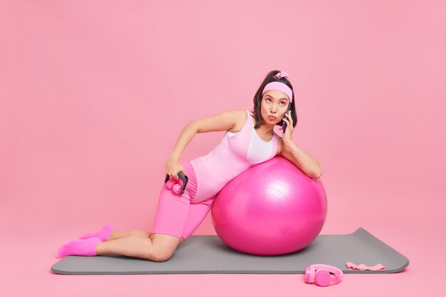 vrouw gebruikt stimulator leunt op fitnessbal heeft telefoongesprek ergens geconcentreerd doet regelmatig oefeningen thuis geïsoleerd op roze
