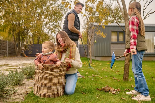 Vrouw gehurkt aanraken kind in mand en familie in tuin