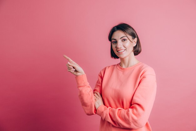 Vrouw, gekleed in casual trui op achtergrond blij gezicht lachend kijken naar de camera. Wijs met wijsvinger naar links.