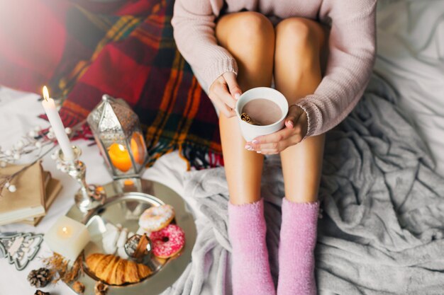 vrouw geniet van de ochtendtijd in haar bed, met warme, gezellige wollen trui en roze sokken, met grote kop koffie.