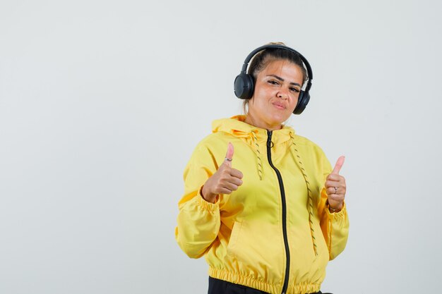 Vrouw genieten van muziek met koptelefoon, duimen uo in sport pak vooraanzicht.