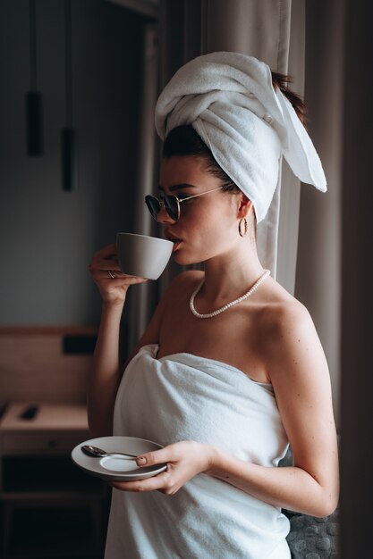 Vrouw gewikkeld in een handdoek na een douche drinken koffie