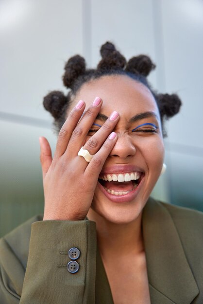 vrouw glimlacht breed toont witte tanden maakt gezicht palm geamuseerd door iemand heeft knot kapsel levendige make-up draagt stijlvolle kleding poses