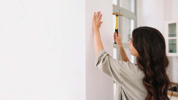 Vrouw hameren nagel aan de muur