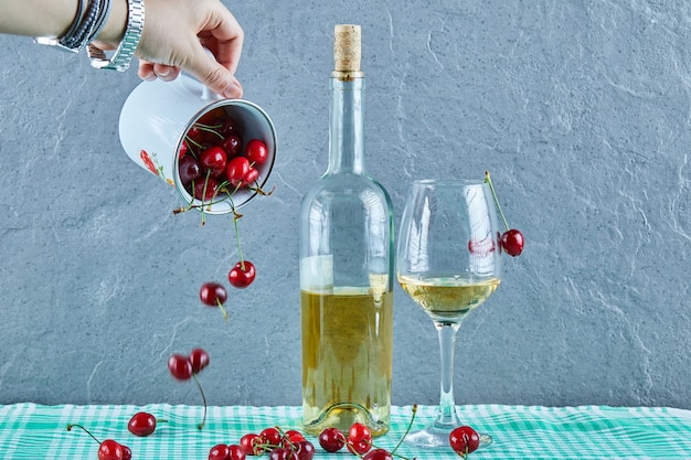 Gratis foto vrouw hand gooien kopje kersen en een fles witte wijn met glas op blauwe ondergrond