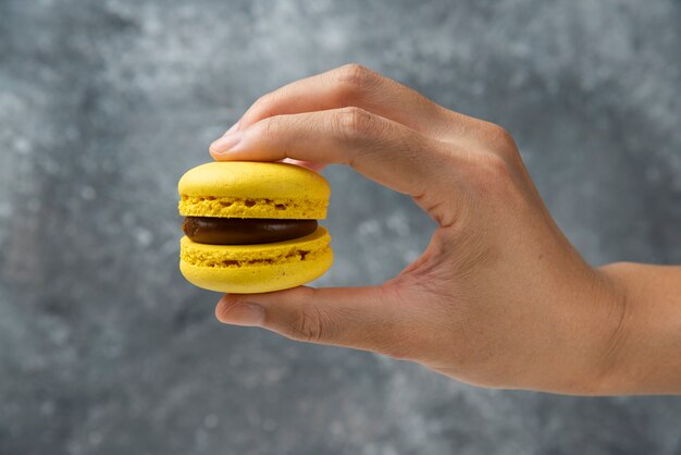 Vrouw hand met gele smakelijke macaron op marmeren oppervlak.