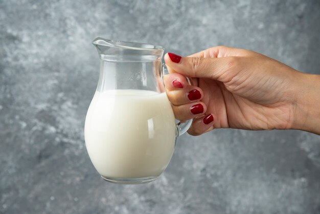 Vrouw hand met glazen pot melk op marmer.