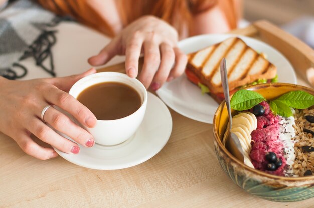 Vrouw hand met kopje thee met sandwich en havermout ontbijt