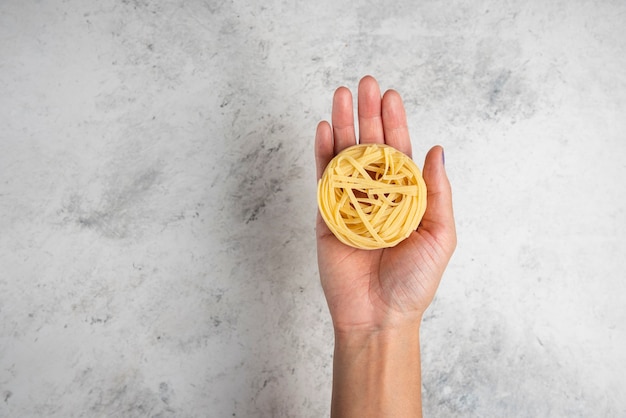 Vrouw hand met rauwe pasta nest op witte achtergrond.