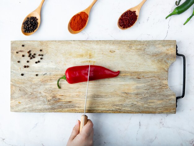 vrouw hand snijden peper op snijplank en kruiden op witte tafel